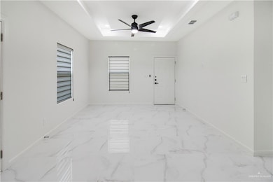 Tiled spare room featuring ceiling fan and a raised ceiling