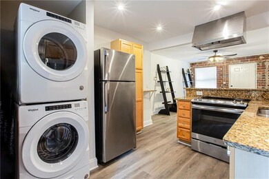 Kitchen with appliances with stainless steel finishes, wall chimney range hood, stacked washer / drying machine, light wood finished floors, and light brown cabinetry