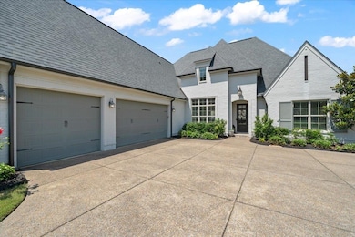 French country home featuring a shingled roof, driveway, brick siding, and an attached garage