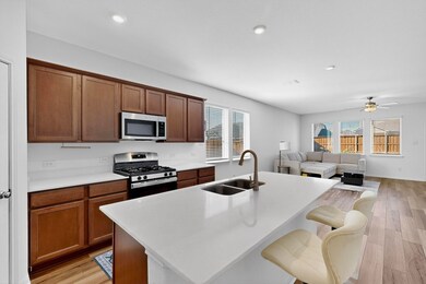 Kitchen with light wood-style flooring, stainless steel appliances, a kitchen island with sink, open floor plan, and light stone counters