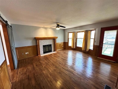 Unfurnished living room featuring a barn door, a textured ceiling, dark wood finished floors, wainscoting, and a fireplace