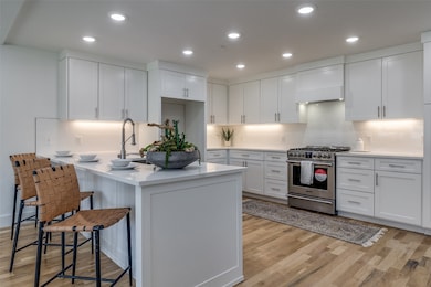 Kitchen with backsplash, gas stove, white cabinetry, a breakfast bar area, and recessed lighting
