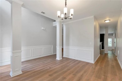 Unfurnished dining area featuring a chandelier, light wood-type flooring, wainscoting, a decorative wall, and decorative columns