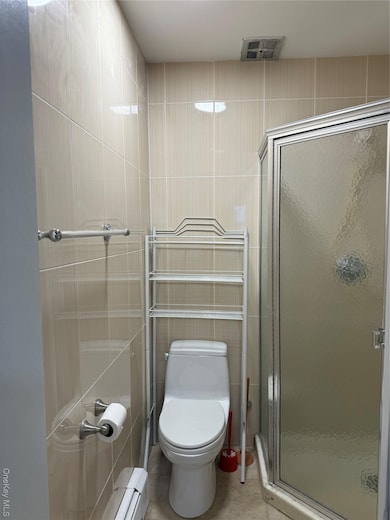 Bathroom with a shower stall, tile walls, a baseboard radiator, and light tile patterned flooring