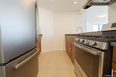 Kitchen with appliances with stainless steel finishes, light tile patterned floors, brown cabinetry, ventilation hood, and a peninsula