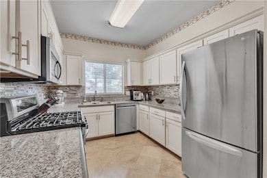 Kitchen with appliances with stainless steel finishes, light stone counters, white cabinetry, and backsplash