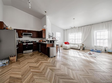 Kitchen with appliances with stainless steel finishes, dark countertops, open floor plan, a chandelier, and hanging light fixtures