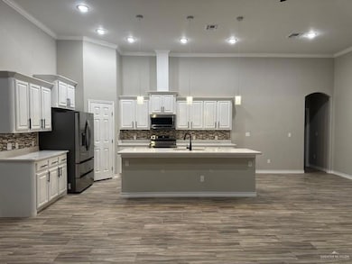 Kitchen featuring white cabinets, arched walkways, a sink, ornamental molding, and appliances with stainless steel finishes