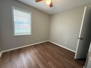 Unfurnished room featuring a ceiling fan, dark wood-style flooring, a textured ceiling, and baseboards