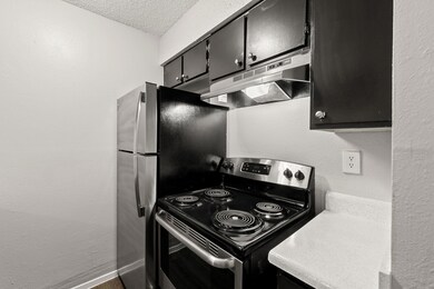 Kitchen featuring stainless steel electric range, dark cabinetry, a textured wall, under cabinet range hood, and light countertops