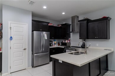 Kitchen featuring visible vents, a peninsula, appliances with stainless steel finishes, dark cabinetry, and wall chimney range hood