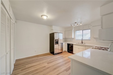 Kitchen featuring white appliances, light wood-type flooring, white cabinetry, and light stone countertops