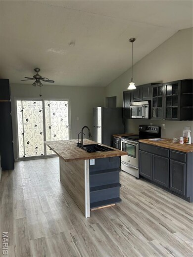 Kitchen featuring wood counters, stove, a center island with sink, glass insert cabinets, and vaulted ceiling