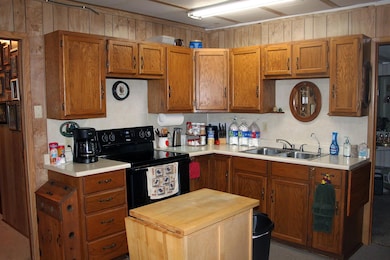 Kitchen featuring black electric range oven, brown cabinetry, wood walls, and butcher block counters