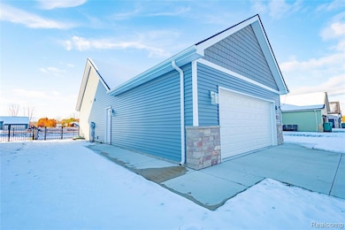 View of snowy exterior with a garage and stone siding