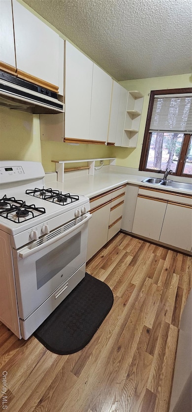 Kitchen featuring white cabinetry, white stove, light wood-style flooring, light countertops, and range hood