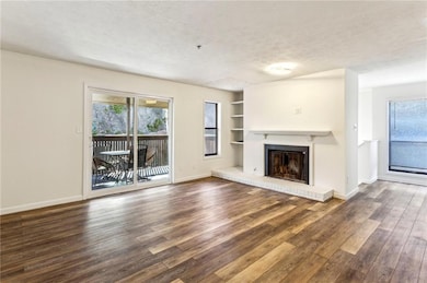 Unfurnished living room with dark wood-style flooring, a healthy amount of sunlight, a fireplace, and a textured ceiling