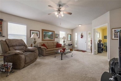 Living room featuring carpet, a ceiling fan, and vaulted ceiling