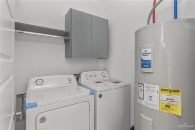 Clothes washing area featuring cabinet space, water heater, and washing machine and dryer
