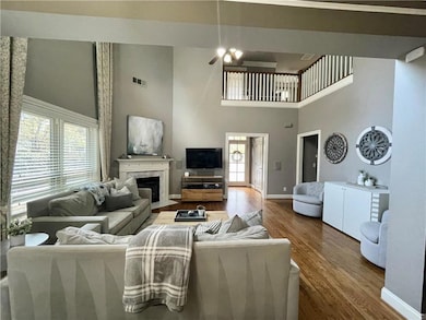 Living room with a towering ceiling, baseboards, wood finished floors, a ceiling fan, and a high end fireplace