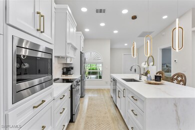 Kitchen with white cabinets, appliances with stainless steel finishes, light wood finished floors, light stone countertops, and decorative light fixtures