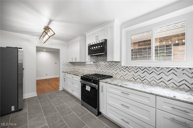 Main kitchen with stainless steel appliances, backsplash, white cabinets, and light stone countertops