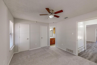 Unfurnished bedroom with light carpet, a textured ceiling, ensuite bathroom, and ceiling fan