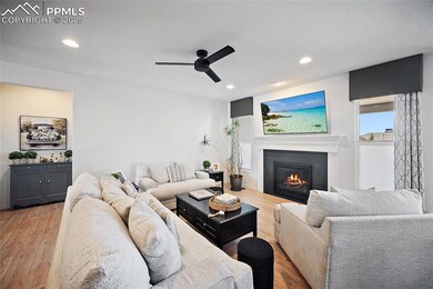 Living room featuring a tiled fireplace, a ceiling fan, light wood finished floors, and recessed lighting