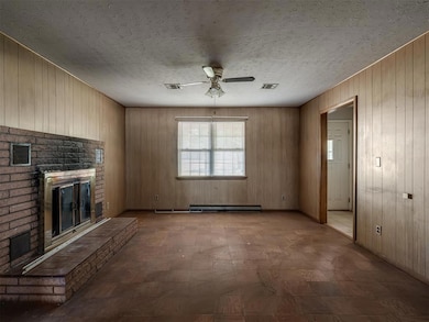 Unfurnished living room with wooden walls, a brick fireplace, ceiling fan, and a textured ceiling