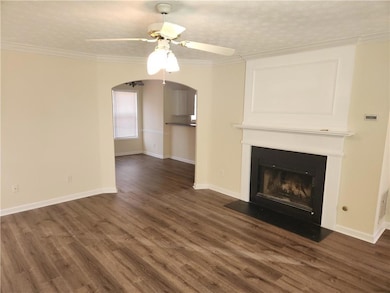 Unfurnished living room featuring a ceiling fan, wood finished floors, a large fireplace, baseboards, and ornamental molding