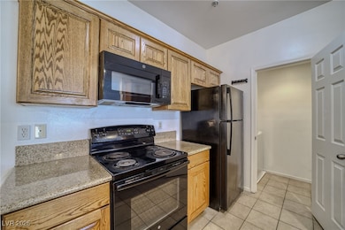 Kitchen featuring black appliances, light tile patterned flooring, light stone counters, and brown cabinetry