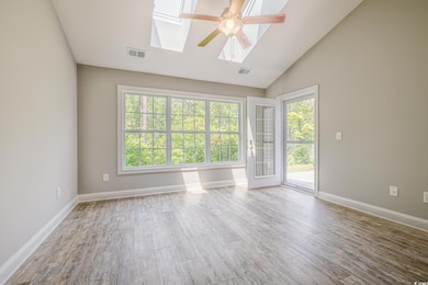Empty room featuring a skylight, ceiling fan, wood finished floors, baseboards, and high vaulted ceiling