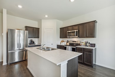 Kitchen featuring stainless steel appliances, dark brown cabinetry, dark wood-style floors, a kitchen island with sink, and recessed lighting