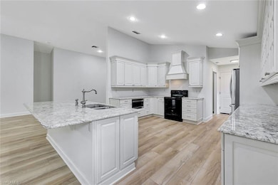 Kitchen featuring black / electric stove, premium range hood, light wood finished floors, white cabinets, and recessed lighting