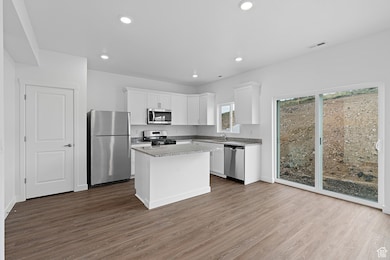 Kitchen featuring appliances with stainless steel finishes, white cabinets, dark wood-type flooring, recessed lighting, and a kitchen island