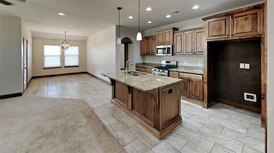 Kitchen with light stone countertops, hanging light fixtures, a center island with sink, recessed lighting, and stainless steel appliances