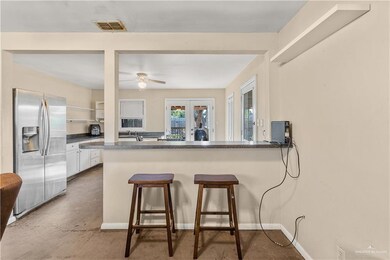 Kitchen featuring stainless steel refrigerator with ice dispenser, white cabinets, a kitchen bar, concrete flooring, and kitchen peninsula