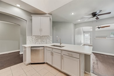 Kitchen featuring stainless steel dishwasher, decorative backsplash, a peninsula, ceiling fan, and light tile patterned flooring