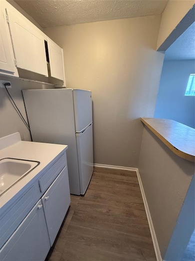 Kitchen with a textured ceiling, light countertops, dark wood finished floors, white cabinets, and white refrigerator