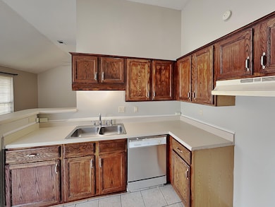 Kitchen with light countertops, light tile patterned floors, under cabinet range hood, and vaulted ceiling