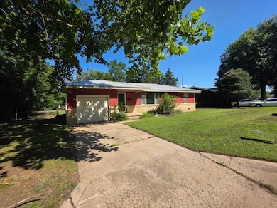 Single story home with a garage, concrete driveway, a front yard, and a metal roof