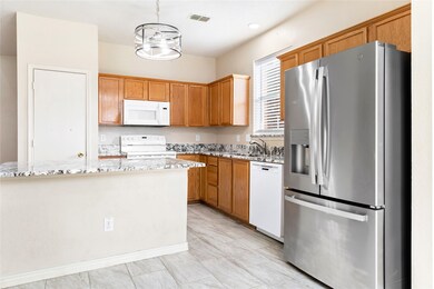 Kitchen with white appliances, light stone countertops, hanging light fixtures, an island with sink, and brown cabinets