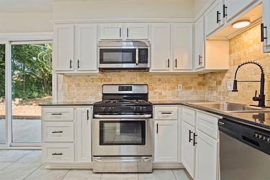 Kitchen featuring stainless steel appliances, white cabinetry, and tasteful backsplash