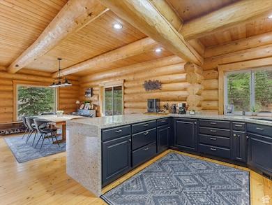 Kitchen featuring pendant lighting, light wood finished floors, light stone countertops, a wood ceiling with exposed beams, and log walls