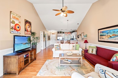 Living room with wainscoting, light wood-style floors, a ceiling fan, and high vaulted ceiling