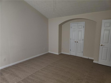 Unfurnished bedroom featuring arched walkways, carpet floors, vaulted ceiling, baseboards, and a textured ceiling