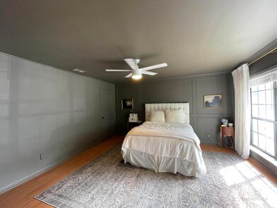 Bedroom with a decorative wall, visible vents, ceiling fan, and wood finished floors