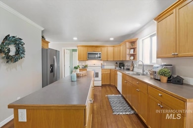 Kitchen with ornamental molding, appliances with stainless steel finishes, a center island, wood finished floors, and open shelves