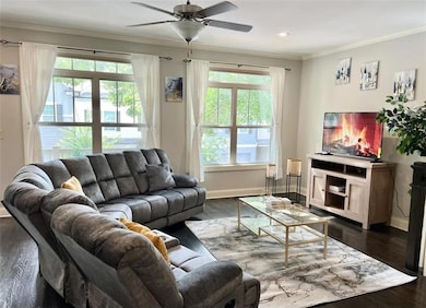 Living room with ornamental molding, dark wood-style floors, and a ceiling fan