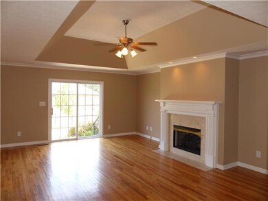 The living room has a fireplace, a tray ceiling, a sliding glass door to the patio, and gleaming hardwood floors. 
